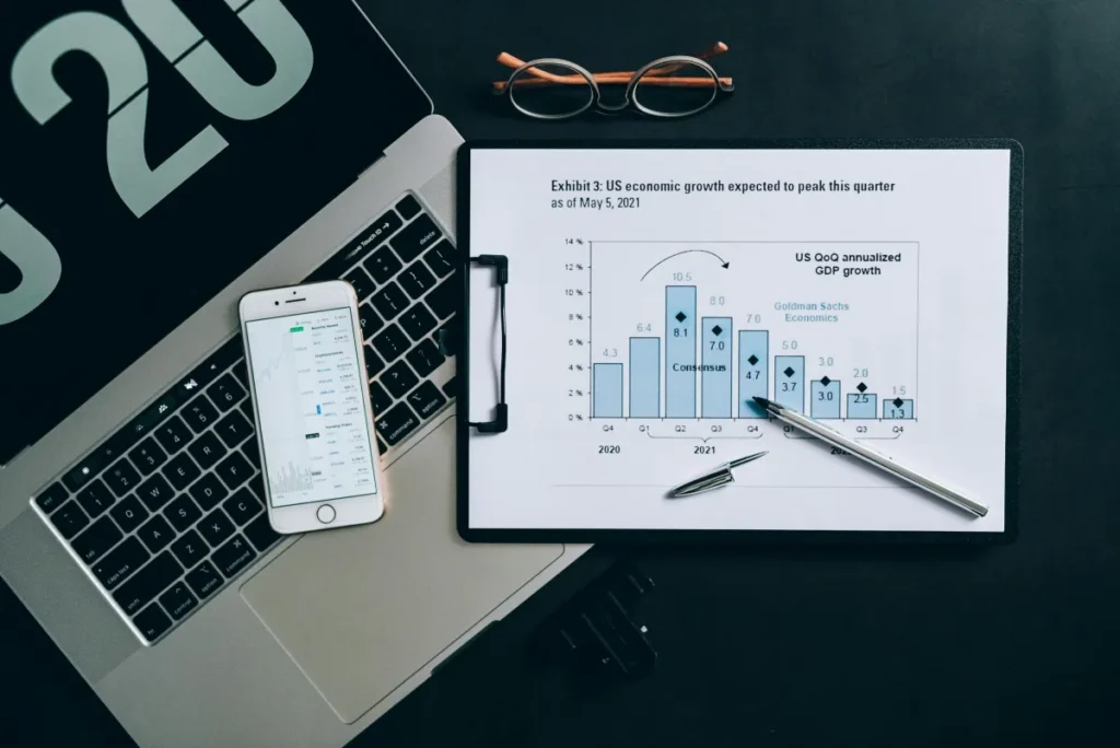 Tampilan dari atas meja analisis data ekonomi dengan laptop, grafik, dan dokumen laporan keuangan