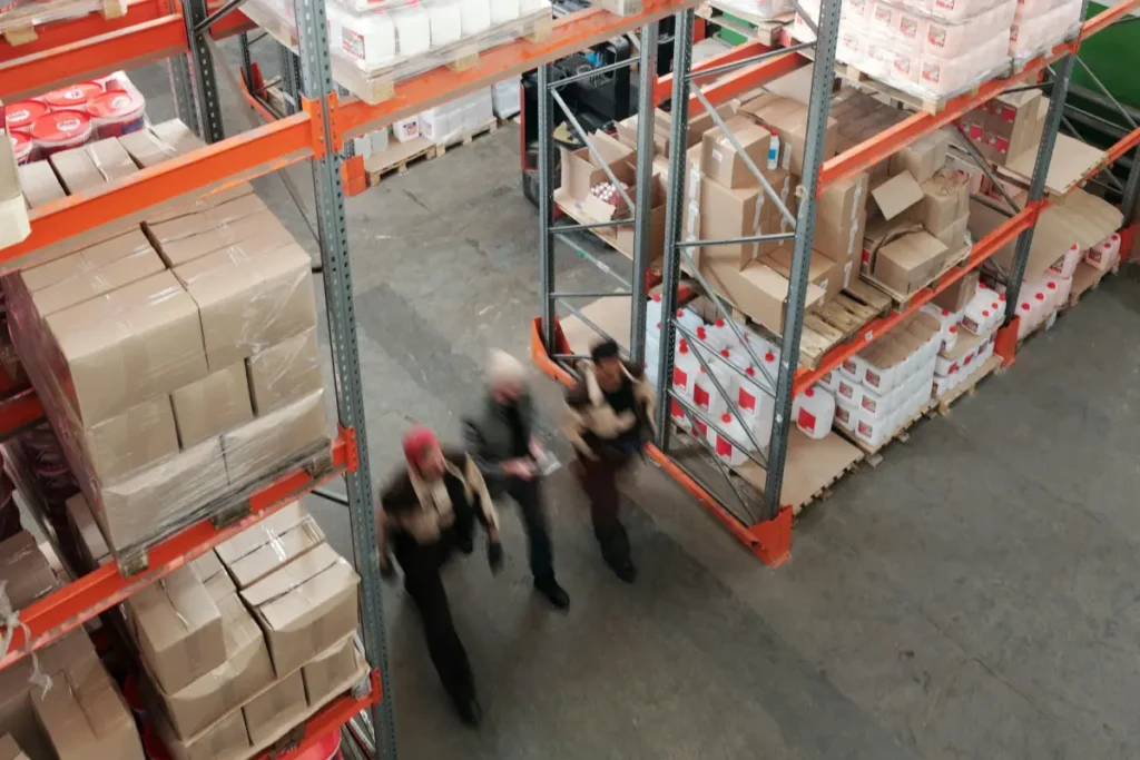 Pekerja gudang sibuk beraktivitas di antara rak-rak penuh kotak dalam fasilitas logistik modern